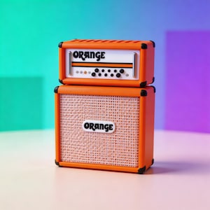 May include: A miniature orange guitar amplifier with the word "ORANGE" displayed on the top and bottom. The amplifier has a speaker grill and black accents. The top section has knobs and a white panel.