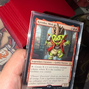 May include: A Krenko, Mob Boss trading card in a clear plastic protective sleeve. The card features a green goblin character wearing a crown and red coat, holding a dagger. The text reads Krenko, Mob Boss, Legendary Creature - Goblin Warrior.