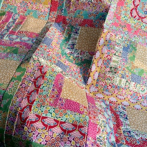 Pode incluir: Um cobertor de retalhos colorido com uma variedade de padrões florais em tons de rosa, verde, azul e amarelo. O cobertor é feito de quadrados e retângulos, e as costuras são visíveis.