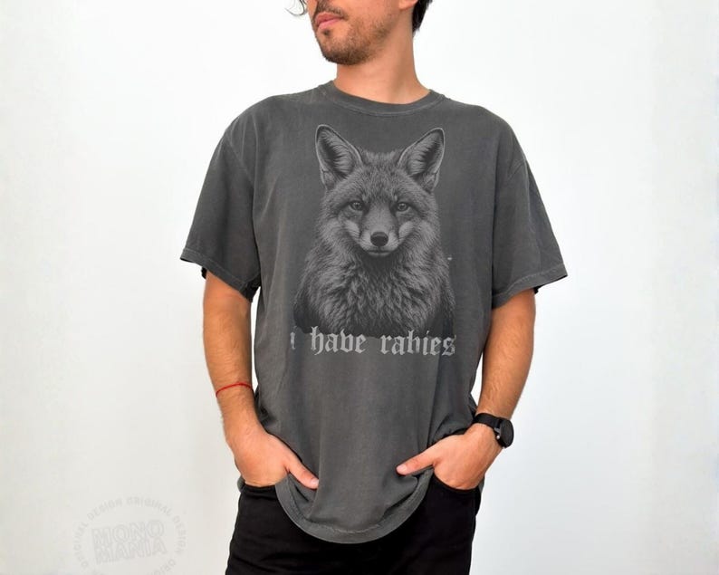 May include: A charcoal gray short-sleeve t-shirt featuring a detailed monochromatic illustration of a fox head centered on the chest. Below the fox graphic, the text "I have rabies" is printed in a stylized, gothic-inspired white font.