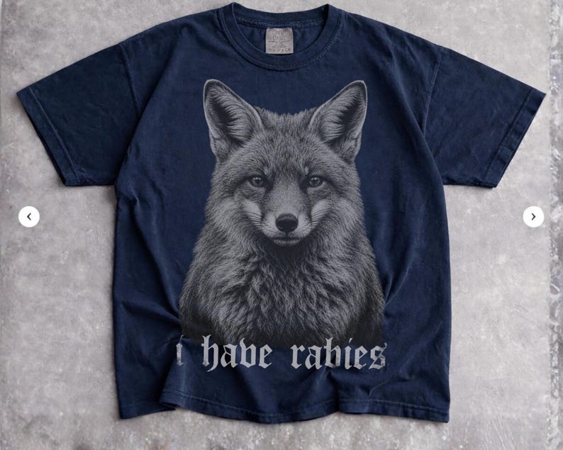 May include: A dark navy blue short-sleeve t-shirt featuring a detailed, centered graphic of a fox head in shades of gray. Below the fox illustration, the text "I have rabies" is printed in a white, gothic-style font across the chest area.
