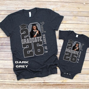 May include: Dark grey t-shirts and a onesie with a graduation theme. The shirts feature a photo of a graduate, the year "26", and the words "Graduate" and "Proud Daddy of A" or "Proud Brother of A". The text "Dark Grey" is also visible.