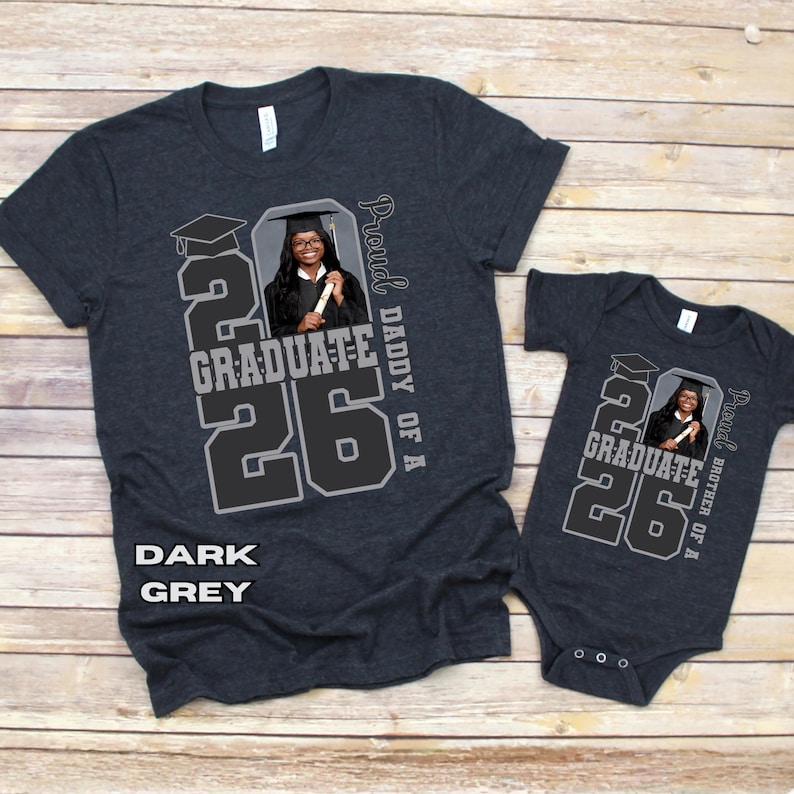 May include: Dark grey t-shirts and a onesie with a graduation theme. The shirts feature a photo of a graduate, the year "26", and the words "Graduate" and "Proud Daddy of A" or "Proud Brother of A". The text "Dark Grey" is also visible.