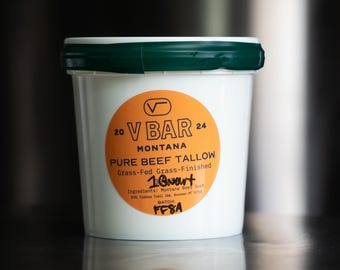 May include: A white plastic container with a dark green lid featuring a round orange label. The label reads V BAR MONTANA PURE BEEF TALLOW, Grass-Fed Grass-Finished, 1 Quart, Ingredients: Montana Beef Suet, and BATCH: FF8A with the years 20 and 24.