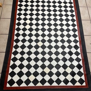 May include: Black and white checkered rug with a red border. The rug has a diamond pattern.