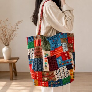 Könnte beinhalten: Eine große Tragetasche mit einem lebendigen Patchwork-Design aus verschiedenen rechteckigen Stoffbahnen in Rot-, Blau-, Grün- und Gelbtönen. Die Tasche zeigt vielfältige Muster, darunter Zickzacklinien, florale Motive und geometrische Formen mit zwei Trageriemen.