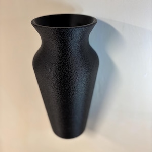 May include: A black ceramic vase with a textured surface. The vase is narrow at the top and widens towards the bottom.