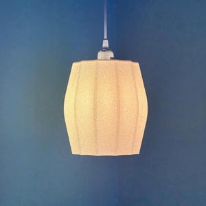 May include: A beige pendant light with a textured, ribbed lampshade. The light hangs from a white cable against a blue backdrop. The lampshade has a cylindrical shape with a slightly curved profile.