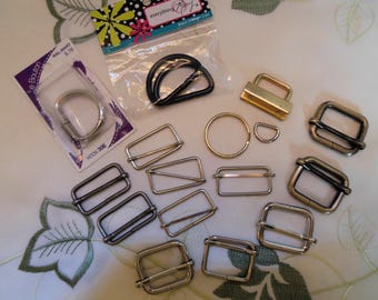 May include: Assortment of silver and gold metal hardware for crafting, including D-rings, slider buckles, and a hook. The hardware is arranged on a white surface with green floral fabric in the background.