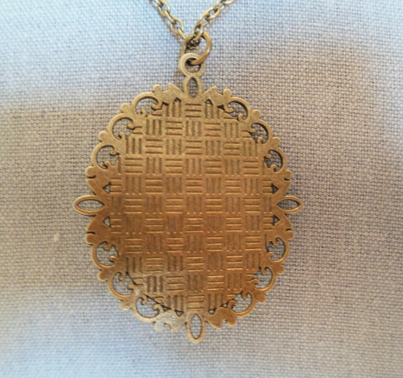 Może przedstawiać: Złoty naszyjnik z wisiorem w kształcie owalu, ozdobiony dekoracyjnym wzorem filigranowym. Wisiorek ma fakturowaną powierzchnię.