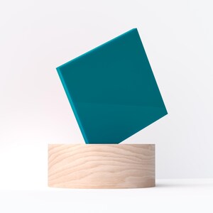 May include: A teal square hovers above a light wood cylinder on a white background. The square is angled, creating a dynamic composition. The wood grain of the cylinder is visible. The overall aesthetic is minimalist and modern.
