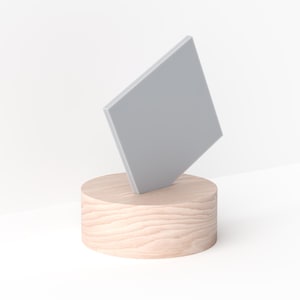 May include: A light gray, geometric shape is angled on top of a light brown, wooden cylinder. The wood grain is visible on the cylinder. The background is white.