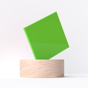 May include: A bright green square balanced on a cylindrical wooden base. The square is angled, creating a modern, minimalist aesthetic against a white background. The wood grain of the base is visible.