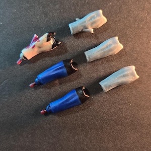 May include: Five different coloured plastic arms for a doll or action figure. The arms are in various shades of blue, grey, and white.