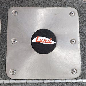 May include: A silver metal plate with a black round button that says "Lund" in red letters on a white background.