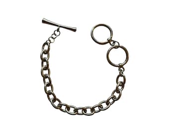 May include: Silver-toned chain bracelet with a T-bar clasp and two connected circular links. The bracelet features a series of oval-shaped links. The jewelry is displayed against a white background.