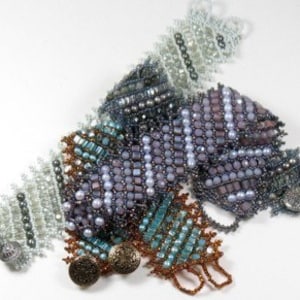 Op de afbeelding: Een verzameling van kralenarmbanden in verschillende tinten blauw, paars en grijs. De armbanden zijn gemaakt met kleine kraaltjes en hebben een geometrisch patroon. Elke armband heeft een knoopsluiting.
