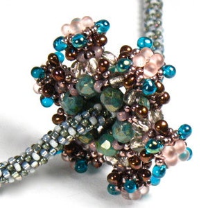 Può includere: Una collana di perline con un gruppo di perline colorate. Il gruppo include perline turchesi, marroni, rosa e trasparenti. Il cordino della collana è un motivo intrecciato di perline argentate, bianche e grigie. Il design è intricato.