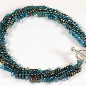 Może przedstawiać: Bransoletka z niebieskich i zielonych koralików z srebrnym zapięciem.