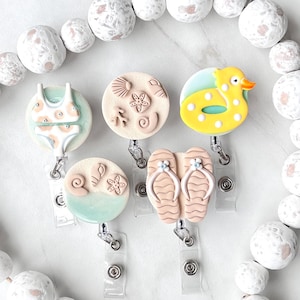 May include: Five colorful summer-themed badge reels with clear plastic clips. The reels feature a swimsuit, seashells, flip flops, and a yellow rubber ducky.