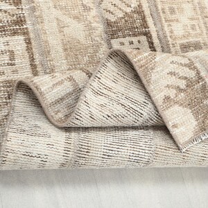 Op de afbeelding: Een opgerolde, rechthoekige vloerkleed met een versleten, vintage uitstraling. Het vloerkleed heeft een patchwork ontwerp in tinten beige, crème en bruin. De randen zijn gerafeld en het is gemaakt van een geweven materiaal.
