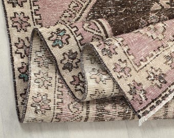 May include: Close-up of a pink and brown patterned rug with a fringed edge. The rug is folded in half, showing the intricate details of the woven design.