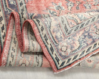 May include: Close-up of a pink and blue patterned rug with a fringed edge. The rug is folded in half, showing the intricate details of the design.