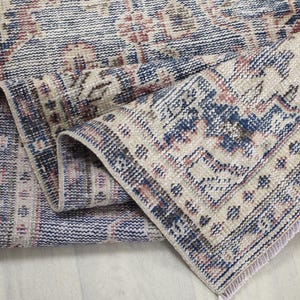 May include: A rolled-up, distressed-look rug with a vintage aesthetic. The rug features a complex pattern in shades of navy blue, beige, and burgundy. The edges are finished with a fringe, and the rug appears to be made of woven material.