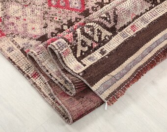 May include: Rolled-up vintage rug with a distressed, faded appearance. The rug features a mix of colors, including shades of pink, brown, and cream. The design includes geometric patterns and a fringed edge, showcasing a traditional style.