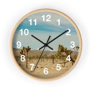 May include: A round wall clock with a wood frame and a desert landscape image. The clock face has white numbers and black hands. The image shows a desert landscape with Joshua trees and a mountain range in the background.
