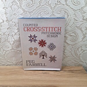 May include: A book titled "Counted Cross-Stitch Patchwork Design" by Peg Farrell. The cover features a blue background with a white title and a variety of colorful cross-stitch designs.