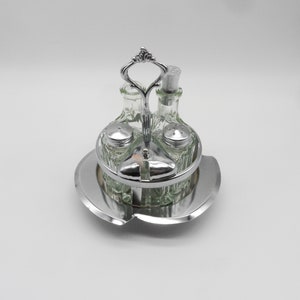 May include: Silver and glass condiment set with four bottles. Two clear glass bottles with silver tops and two smaller salt and pepper shakers. The set sits on a silver tray.