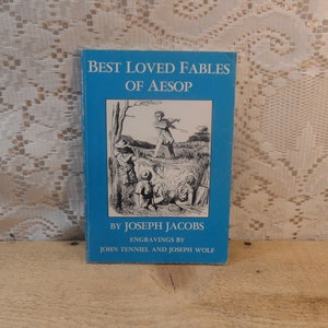 May include: A vintage book titled "Best Loved Fables of Aesop" with a blue cover. The cover features a black and white illustration of people in a field. The author is Joseph Jacobs, with engravings by John Tenniel and Joseph Wolf.