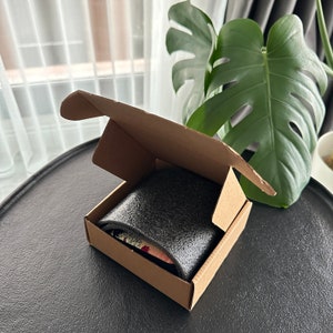 May include: A brown cardboard box with a black foam insert. The box is open and the foam insert is visible. The box is sitting on a black surface.