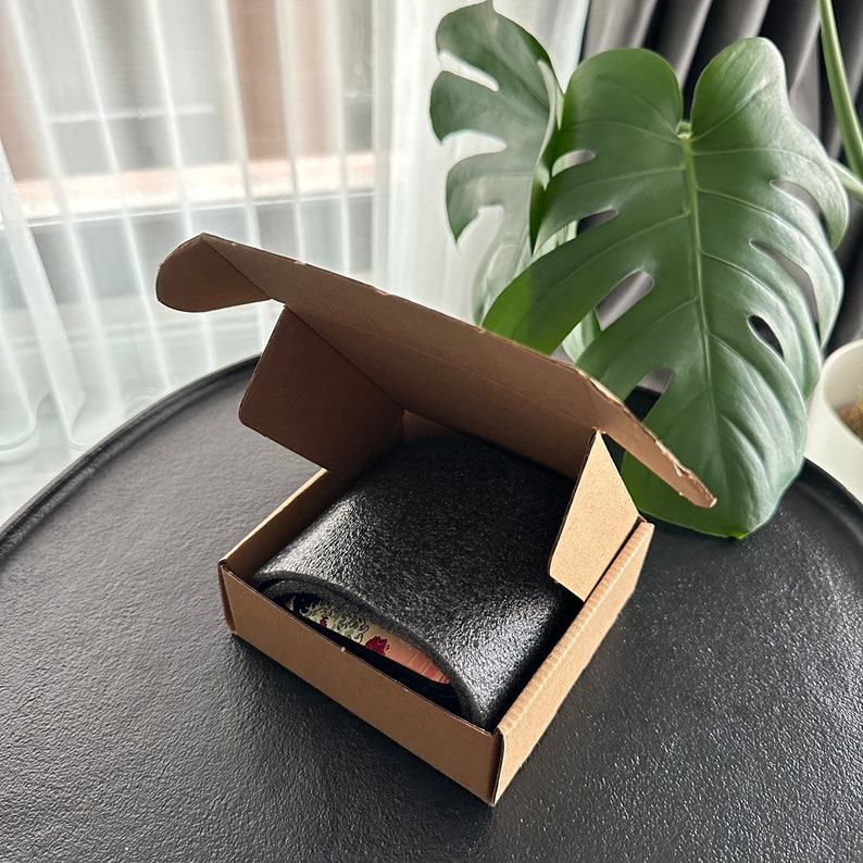 May include: A brown cardboard box with a black foam insert. The box is open and the foam insert is visible. The box is sitting on a black surface.