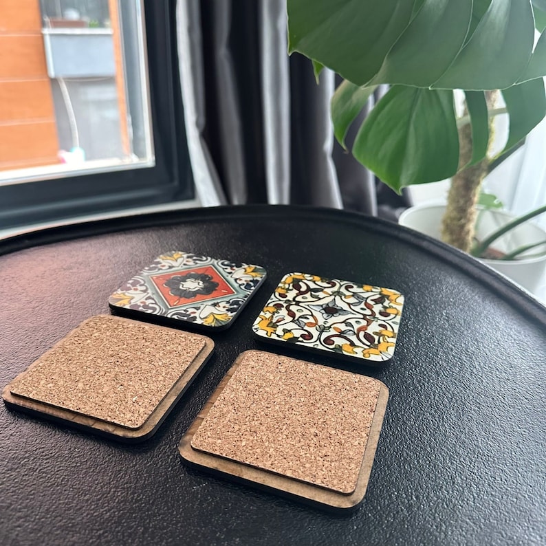 May include: Four square cork coasters with a decorative tile design. The tiles feature a variety of colors and patterns, including red, yellow, blue, and green. The coasters are made of cork and have a wooden frame.