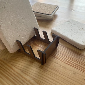 May include: A wooden coaster holder with five slots for storing coasters. The holder is made of dark brown wood and has a rectangular shape. The holder is sitting on a wooden surface.