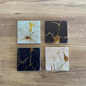 May include: Four square coasters with a cracked design. Two coasters are beige with gold cracks, and two coasters are black with gold cracks.
