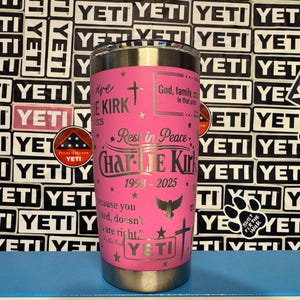 Puede incluir: Un vaso YETI rosa con texto y detalles plateados. El vaso est&aacute; personalizado con el nombre "Charlie Kirk", las fechas 1993-2025 y s&iacute;mbolos religiosos. El fondo presenta una pared de pegatinas y logotipos de YETI.