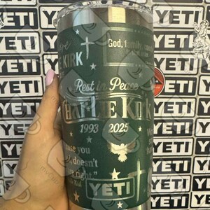 Puede incluir: Un vaso YETI verde con texto y detalles plateados. El texto incluye "Charlie Kirk", "1993-2025", una cruz, estrellas y las palabras "Rest in Peace". El vaso tiene un borde plateado y una tapa transparente.