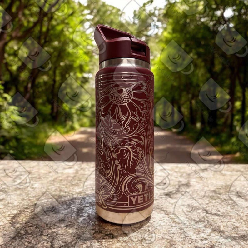 Puede incluir: Una YETI Rambler de color marr&oacute;n con un dise&ntilde;o floral grabado en acero inoxidable. La botella tiene una tapa negra con un asa de bucle.