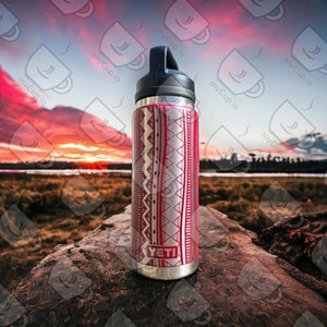 May include: A stainless steel water bottle with a red and white geometric pattern. The bottle has a black lid and the word "YETI" is printed on the bottom. The bottle is sitting on a rock with a blurry background of a sunset.