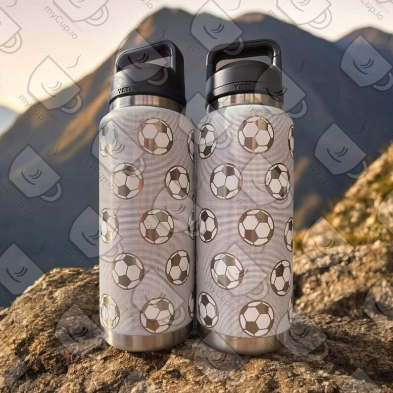 Puede incluir: Dos botellas de agua de acero inoxidable con tapas y asas negras. Las botellas est&aacute;n cubiertas con un patr&oacute;n blanco y gris de balones de f&uacute;tbol.