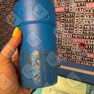 May include: A blue Yeti tumbler with a laser-etched design of waves. The tumbler has a silver lid and the Yeti logo is visible on the side.