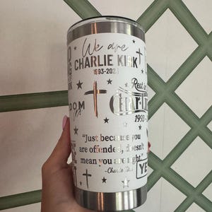 Puede incluir: Un vaso de acero inoxidable blanco con borde y tapa plateados. El vaso presenta texto y gr&aacute;ficos, incluidas las palabras "We are CHARLIE KIRK 1993-2023", cruces y estrellas. Tambi&eacute;n incluye una cita de Charlie Kirk.