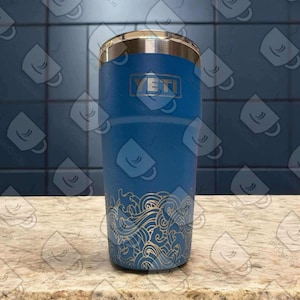 May include: A blue Yeti tumbler with a gold wave design. The tumbler has the Yeti logo on the front.