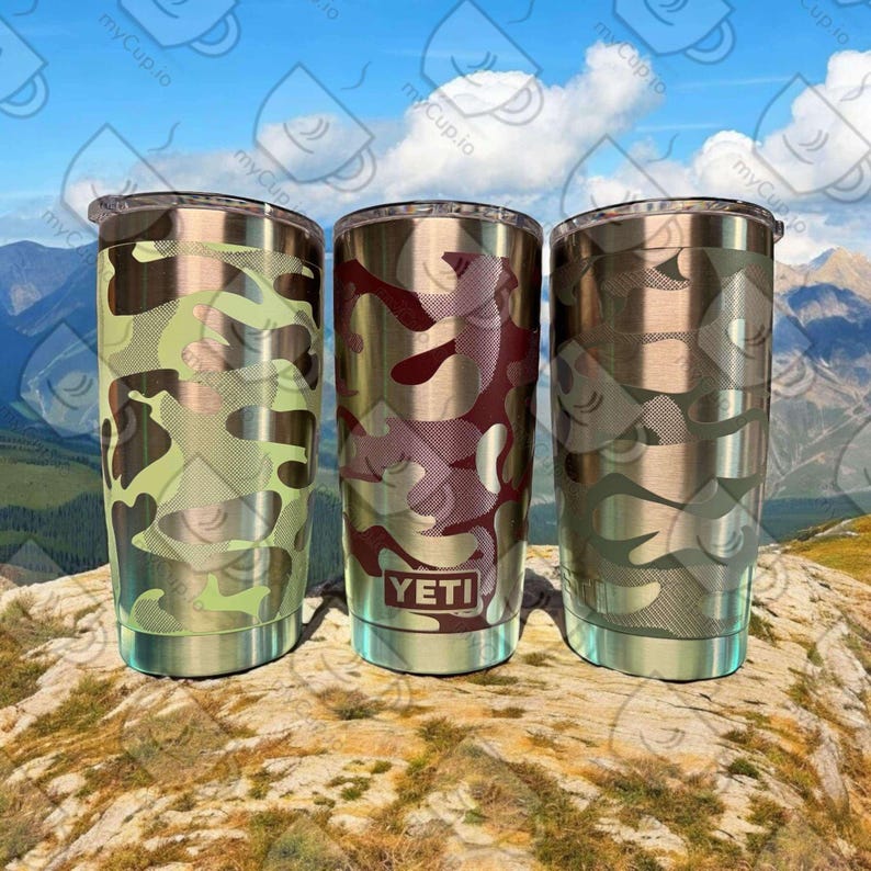 K&ouml;nnte beinhalten: Drei Edelstahlbecher mit verschiedenen Tarnmustern. Die Becher sind alle gleich gro&szlig; und haben die gleiche Form und eine silberne Oberfl&auml;che. Die Becher stehen auf einer felsigen Oberfl&auml;che. Das Wort "YETI" ist auf den mittleren Becher gedruckt.