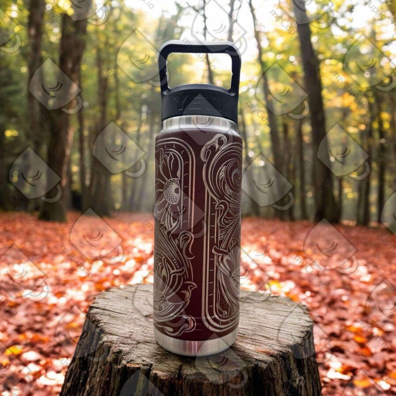 Puede incluir: Una botella de agua de acero inoxidable con tapa y asa negras. La botella tiene una base marr&oacute;n con un dise&ntilde;o floral blanco.