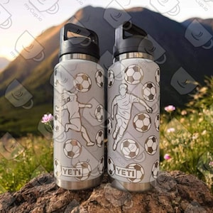 Puede incluir: Dos botellas de agua de acero inoxidable con fondo blanco y un patr&oacute;n de balones de f&uacute;tbol y jugadores. Las botellas tienen tapas y asas negras y la palabra "YETI" est&aacute; impresa en la parte delantera de cada botella.