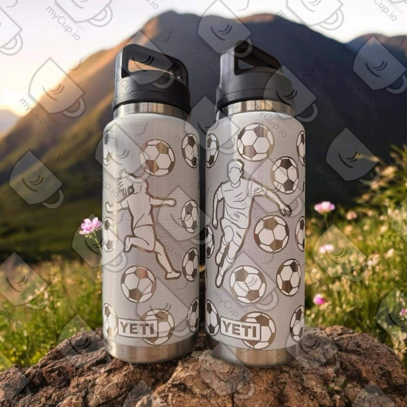 Puede incluir: Dos botellas de agua de acero inoxidable con fondo blanco y un patr&oacute;n de balones de f&uacute;tbol y jugadores. Las botellas tienen tapas y asas negras y la palabra "YETI" est&aacute; impresa en la parte delantera de cada botella.